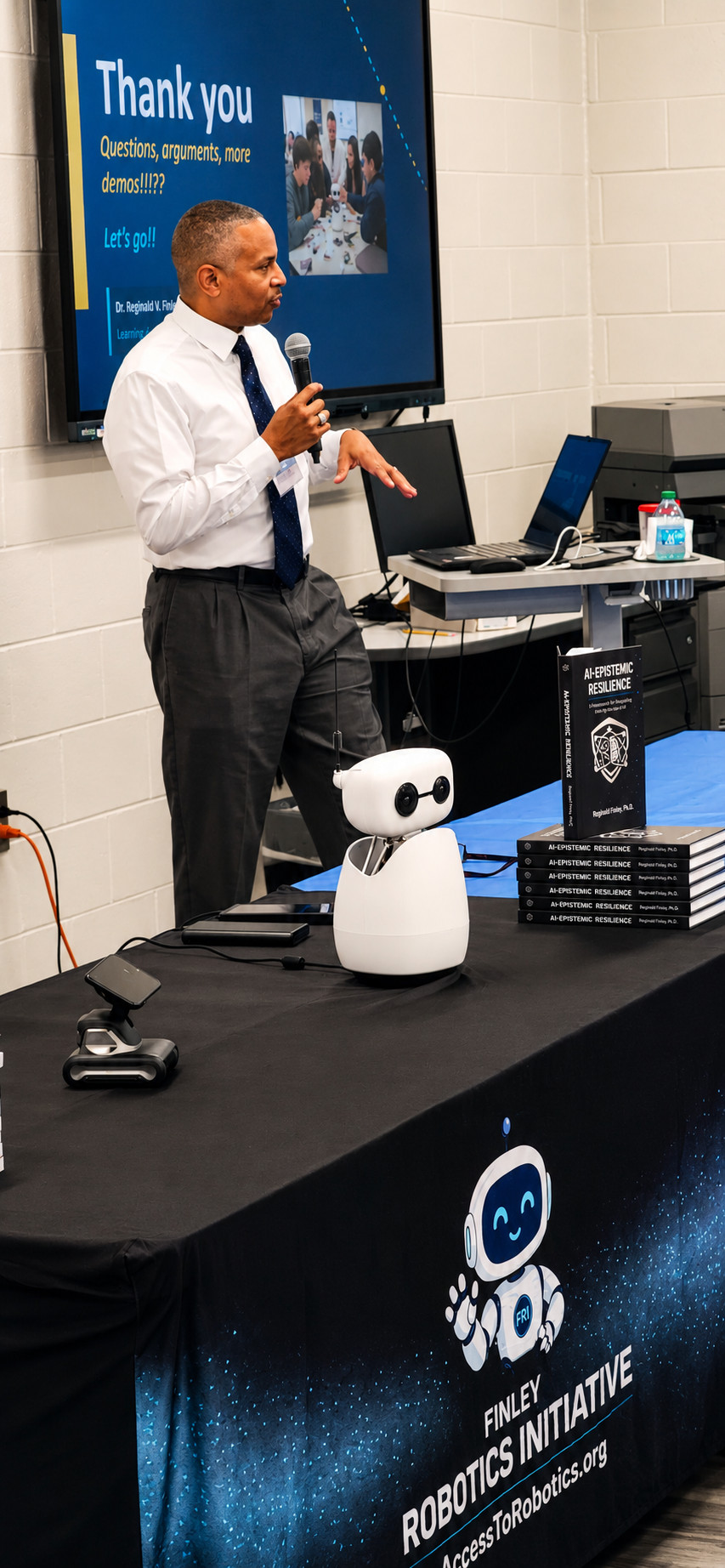 Dr. Finley delivering Smart Tools, Sharper Minds beside a desktop robot and copies of AI-Epistemic Resilience